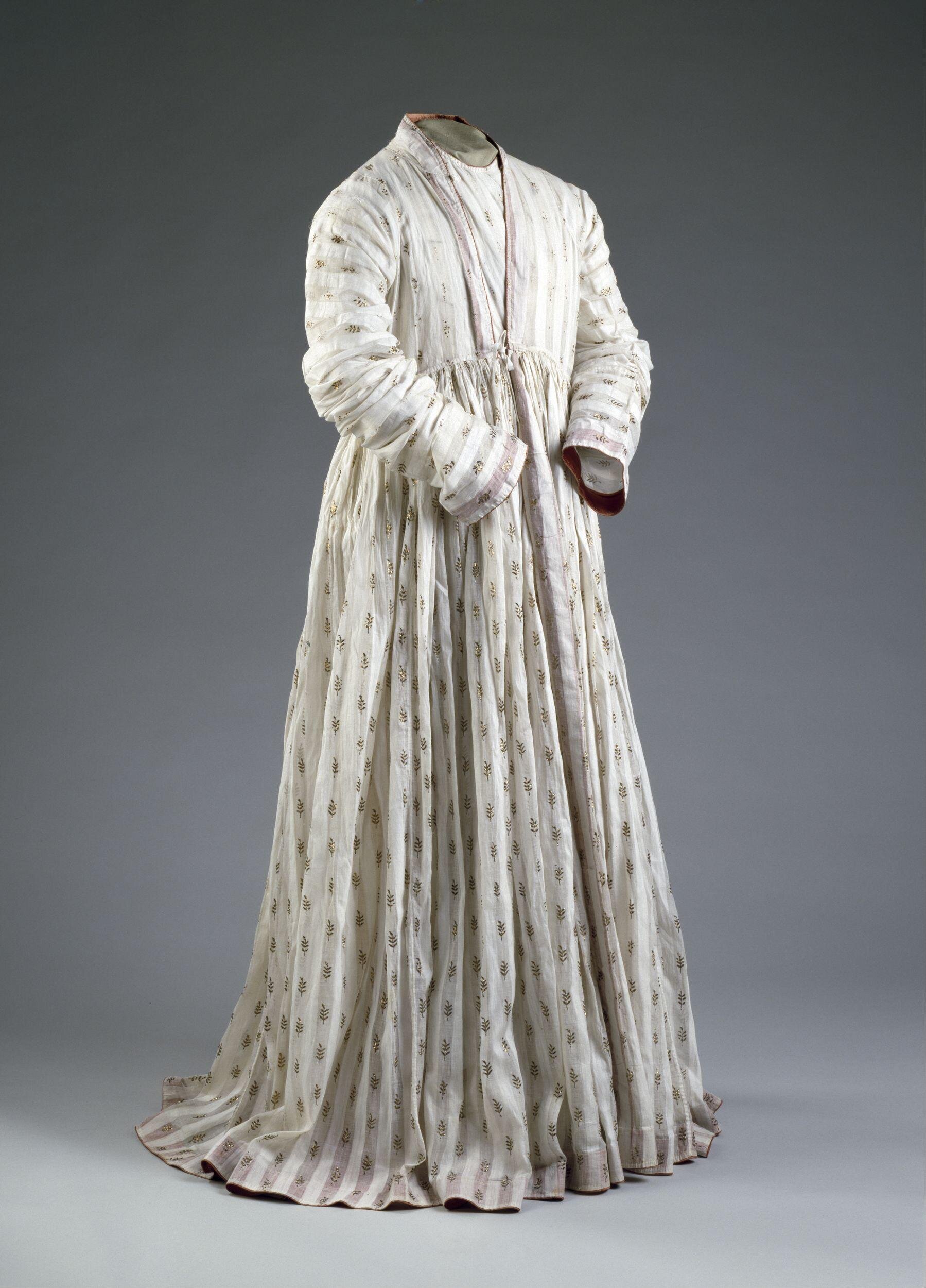 Man's robe (Jama) of white cotton muslin embroidered with gold. Woven in vertical stripes, alternately clear and opaque. The clear stripes are patterned at regular intervals with sprigs of gold foil, applied to the face of the material and stitched down on the reverse with white thread. The hem, collar, cuffs and other borders are faced on the inside with red satin.